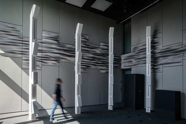 Close-up architectural view of the Immersive Design Lab at ETH Zürich, showcasing custom-engineered white vertical line source loudspeaker enclosures designed by Jürgen Strauss, integrated into a precision wave-field synthesis array above a distinctive textured, wave-patterned acoustic floor design.
