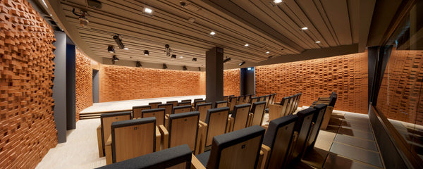 Wide interior view of the ArtLab auditorium at the Max Planck Institute for Empirical Aesthetics in Frankfurt, featuring an acoustic design by Jürgen Strauss with custom floor-to-ceiling brick block diffusion walls, minimalist wood-finished audience seating, and an angled acoustic ceiling layout.