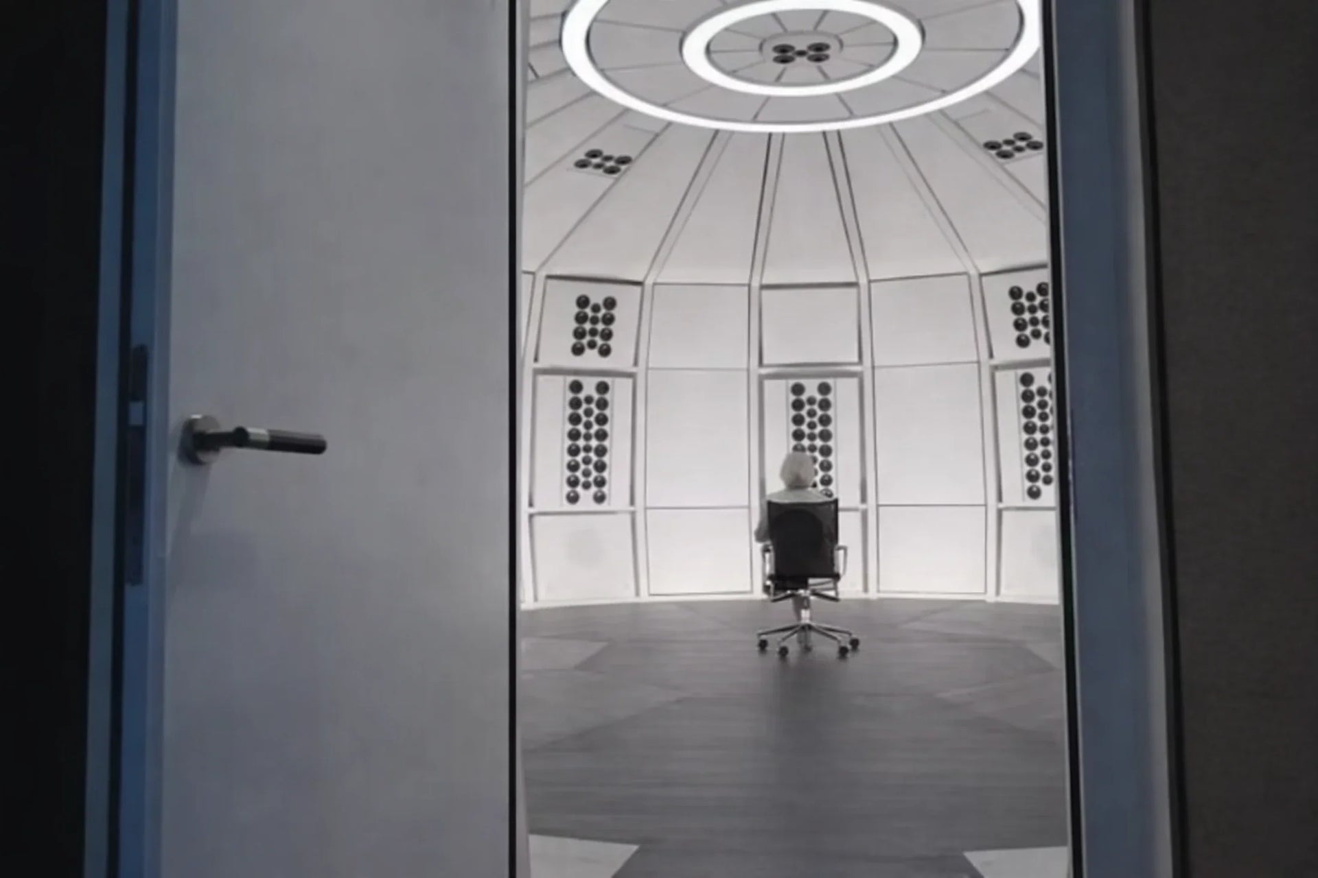 Interior architectural view from an open doorway looking into the precision geometric acoustic dome of THE LAB at SE MUSICLAB, showing an Jürgen Strauss sitting in a studio chair at the central listening position, framed as a cinematic video thumbnail preview for the official SE MUSICLAB brand film.