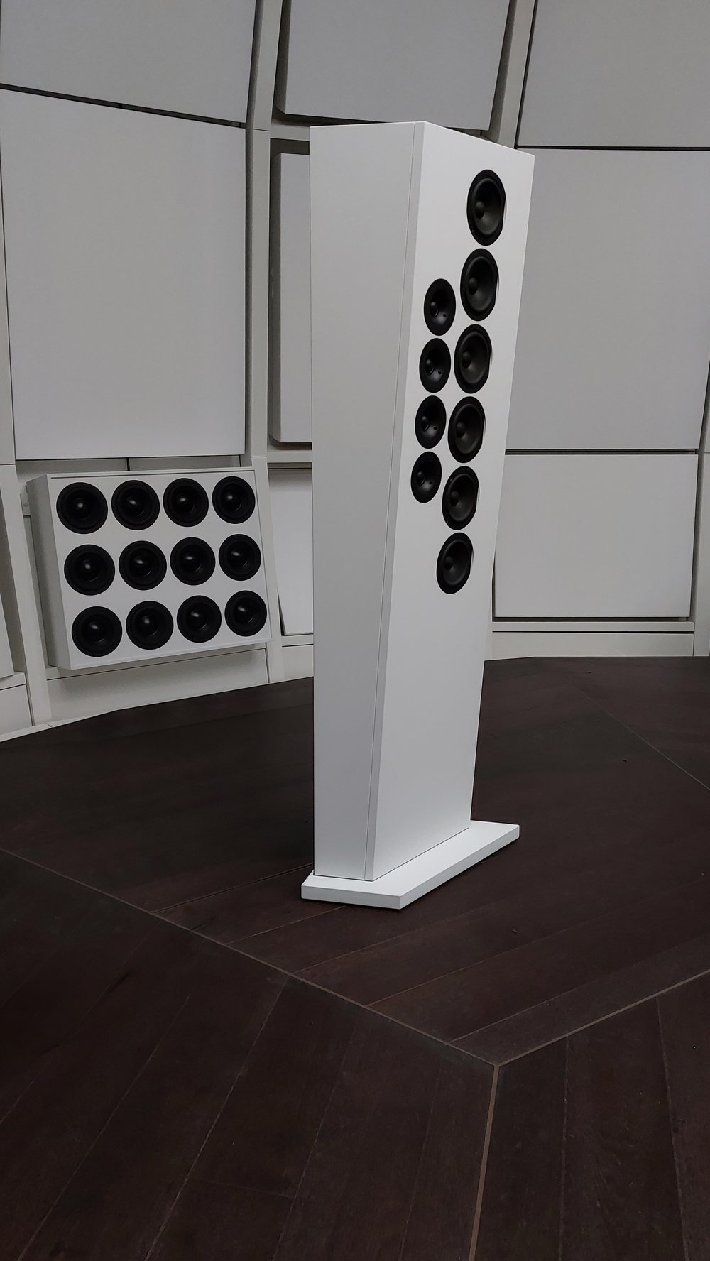 Vertical interior view inside the acoustic environment of THE LAB at SE MUSICLAB in Bern, Switzerland, showcasing a custom white vertical line source loudspeaker tower designed by Jürgen Strauss during system testing, positioned on a dark floor in front of decoupled modular wall acoustic panels.