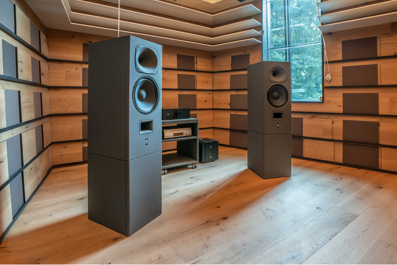 A wide stereo setup of the STRAUSS ELEKTROAKUSTIK SE MF-4 Large-Format Midfield Passive Monitoring Systems mounted on custom stands in a mastering studio with acoustically treated wooden walls and floors, showcasing the matching SE PA-250 power amplifiers and source equipment in an equipment rack between them.