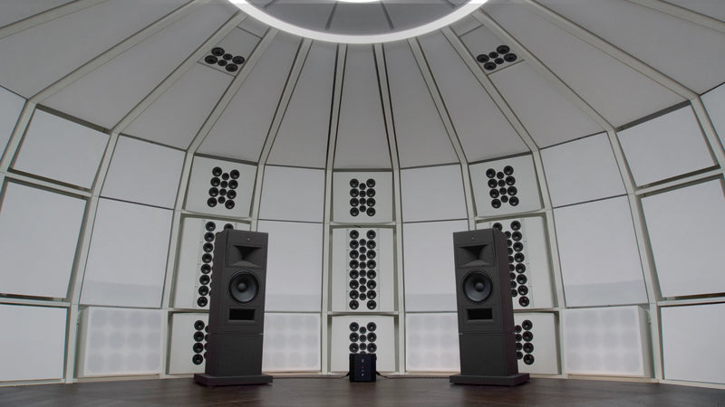 Interior architectural view of the precision-engineered acoustic environment of THE LAB at SE MUSICLAB in Bern, Switzerland, showcasing a pair of massive, custom floor-standing STRAUSS ELEKTROAKUSTIK MF-2.1 main monitors positioned against a custom white decoupled modular wall system beneath a signature multi-ring circular ceiling lighting fixture.